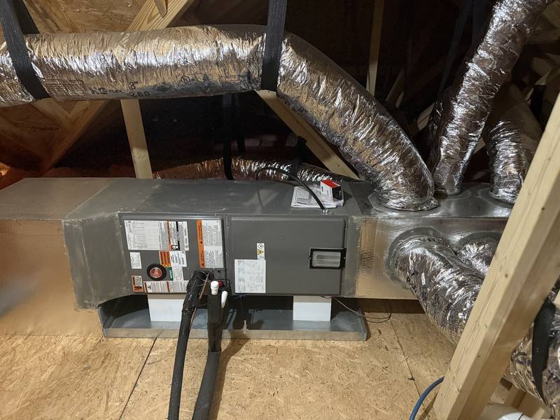 Horizontal Rheem air handler in an attic on a drain pan, with insulated refrigerant lines and silver flex ducts branching off a supply plenum